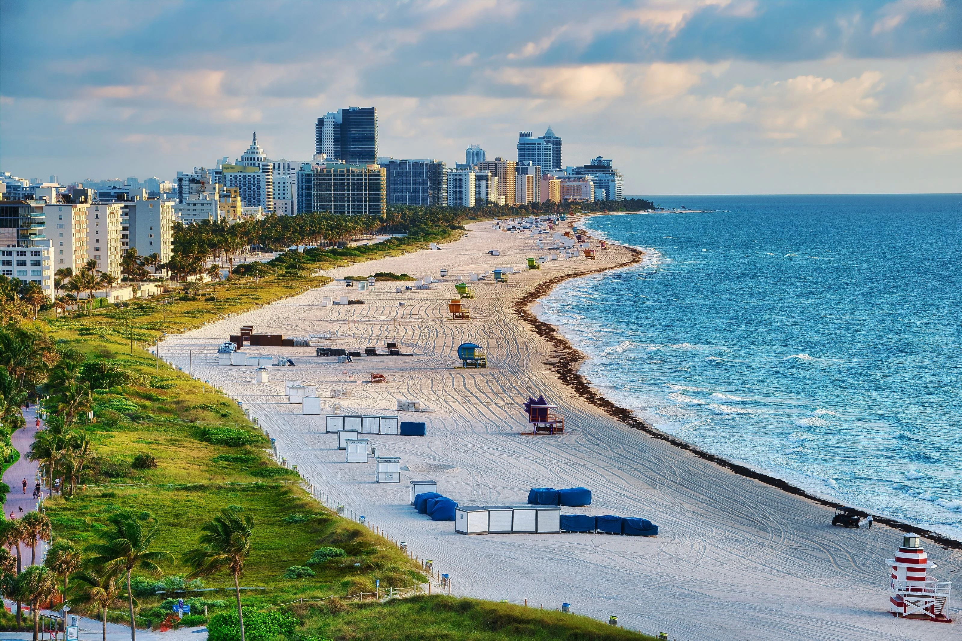 An elevated view along South Beach with Miami Beach's oceanfront skyline, palm trees, white sand, and blue Atlantic water